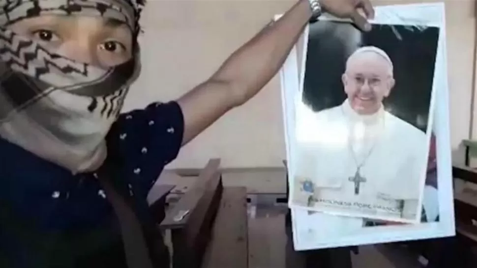 CON LA IMAGEN DEL PAPA. Un terrorista esconde su cara y muestra amenazante una foto de Francisco. 