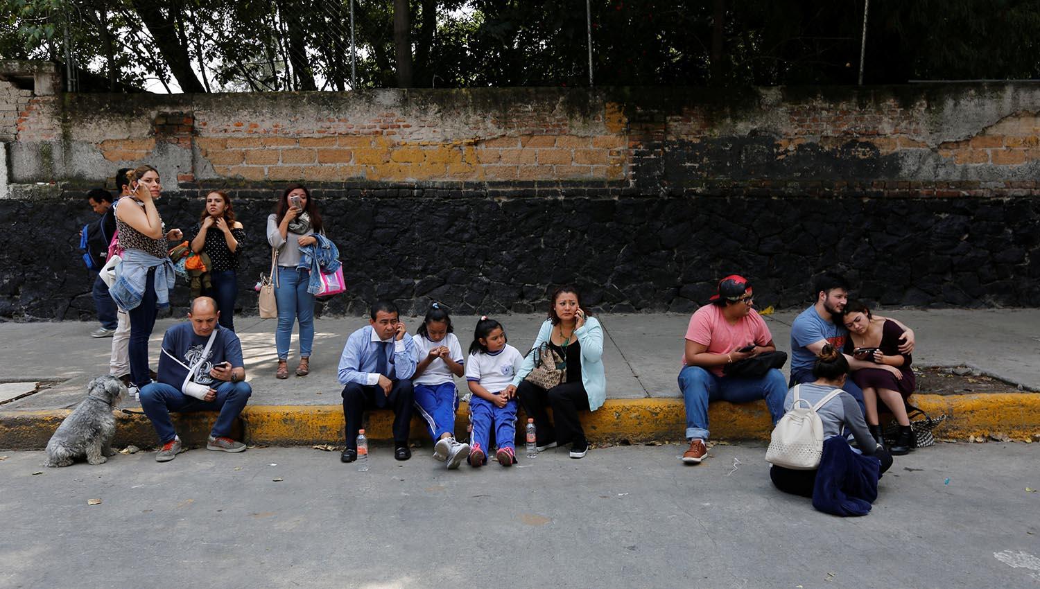 Mayores y chicos, sentados en la vereda tras el sismo. FOTO DE REUTERS. 