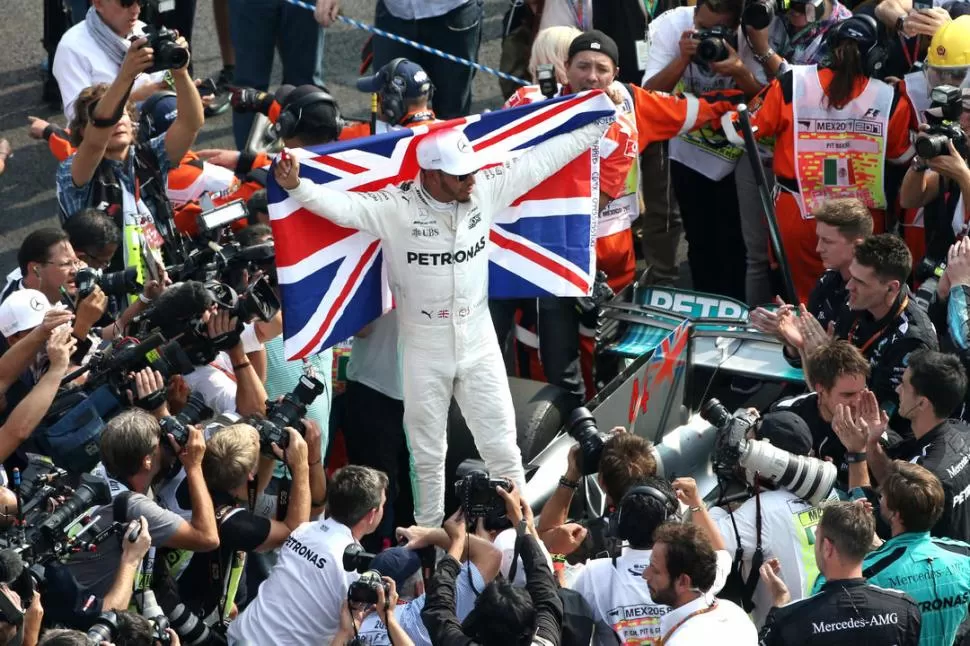      EL MEJOR. Con la carrera terminada, Hamilton salió de su auto y posó con la bandera británica ante el asedio periodístico. corsa