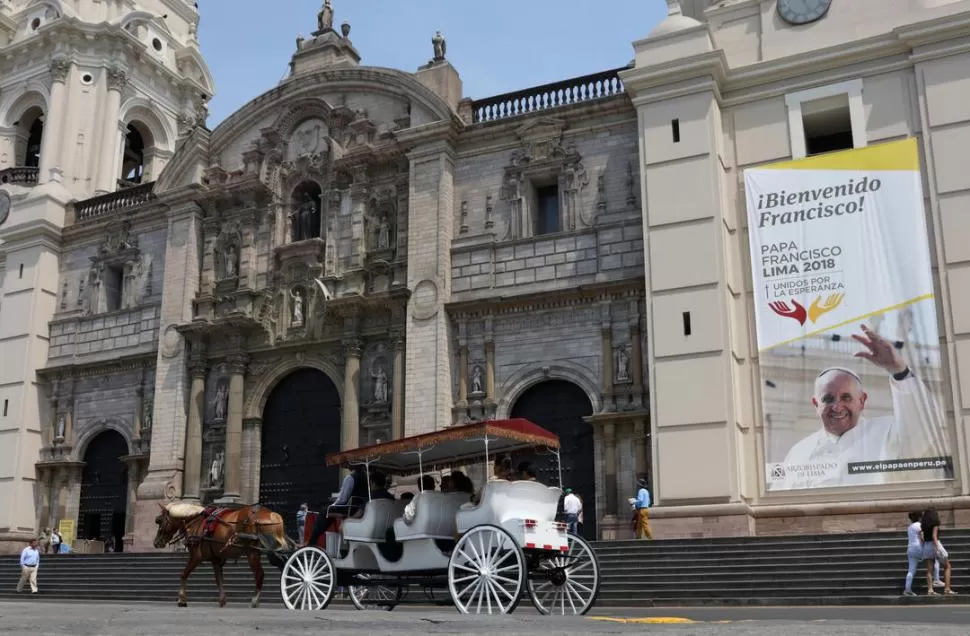 LIMA SE PREPARA. Gente en un carruaje colonial pasa frente a la Catedral, que muestra una gigantesca pancarta. Reuters