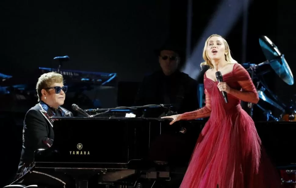 DOS GENERACIONES. Sir Elton John acompañó al piano en el tema “Tiny dancer” a una elegante y sobria Miley Cirus, con un sentador vestido rojo. El músico anunció que se retirará de los escenarios el próximo año. fotos reuters