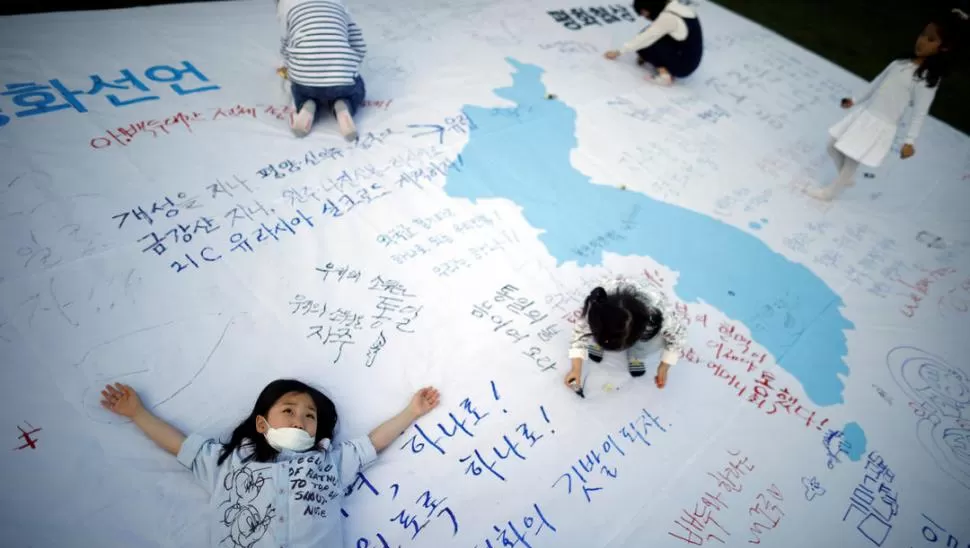 LA UNIFICACIÓN. Unos niños juegan con una bandera de ambas Coreas decorada con mensajes que desean una cumbre exitosa para el viernes 27. Reuters
