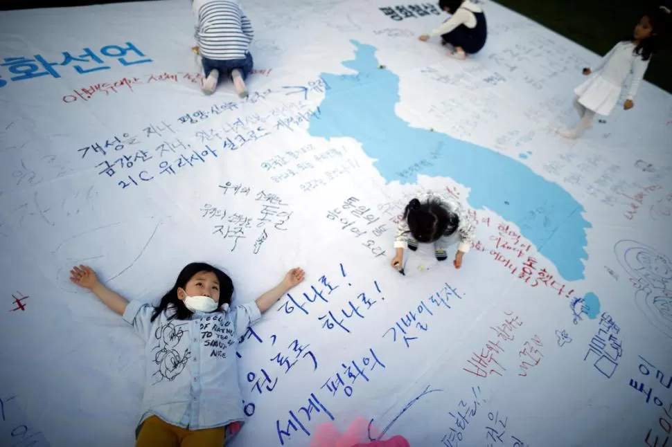 LA UNIFICACIÓN. Unos niños juegan con una bandera de ambas Coreas decorada con mensajes que desean una cumbre exitosa para el viernes 27. Reuters