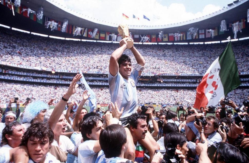 UNA IMAGEN PARA EL RECUERDO. Maradona levanta la Copa mientras es llevado en andas, luego de la final contra Alemania. Atrás, la majestuosidad del estadio Azteca, que se rindió a los pies del “10”.  fifa