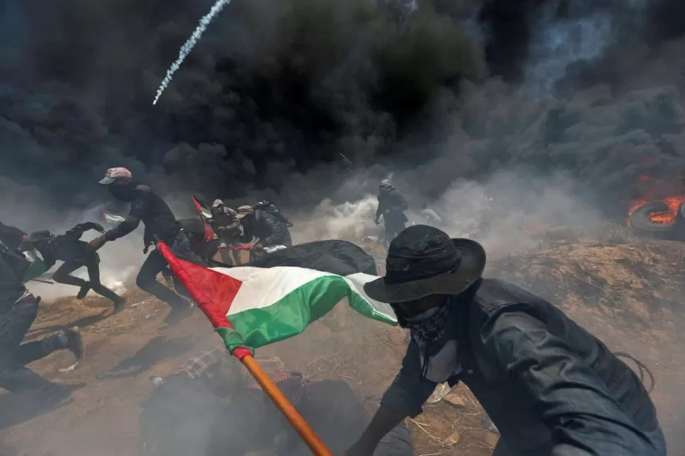 FRONTERA. Jóvenes palestinos corren para ponerse a cubierto de los gases lacrimógenos que lanza el ejército israelí. reuters