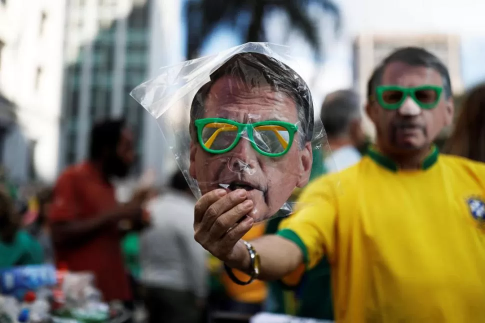 CARETAS. Un vendedor callejero ofrece máscaras con la imagen de Bolsonaro, durante una marcha en San Pablo, a pocos días de los comicios.  reuters 
