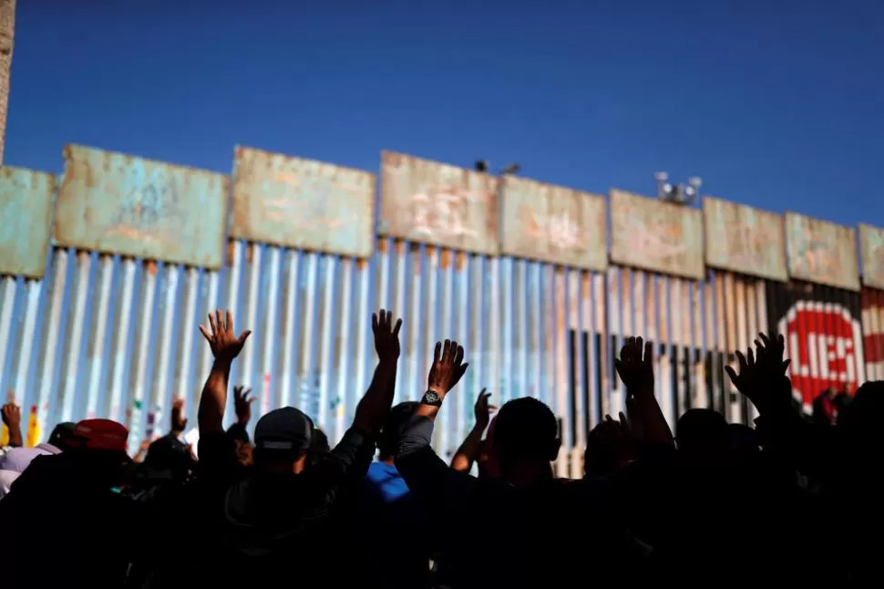 DESESPERADOS. Migrantes rezan en la frontera entre México y EU.  Reuters