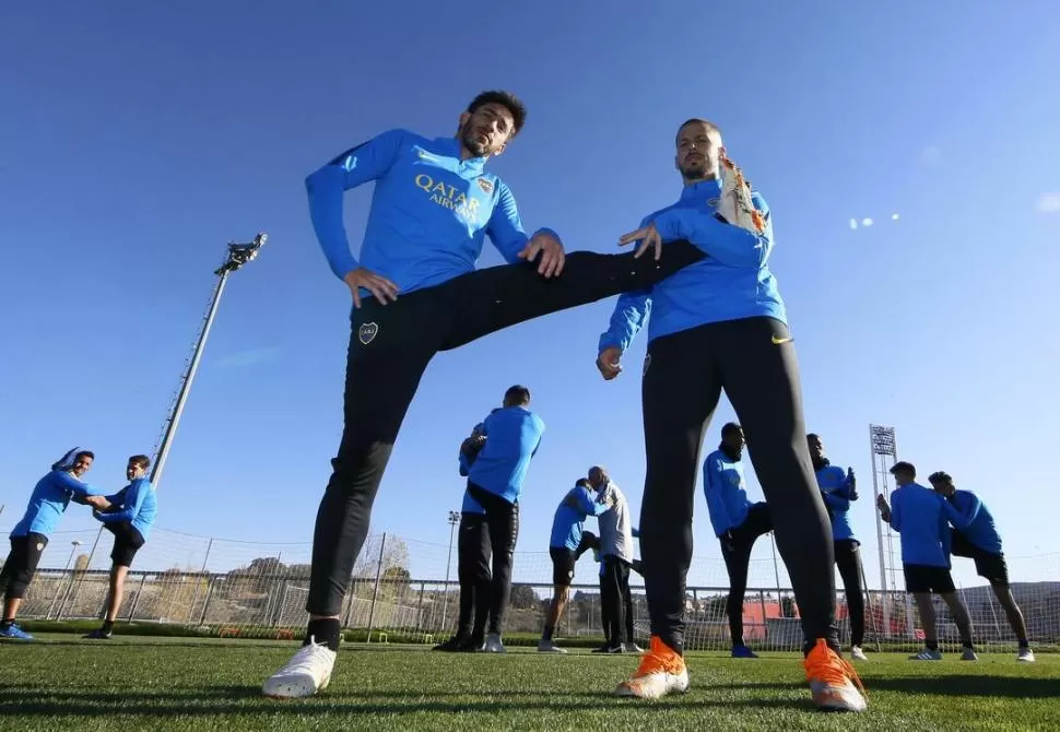 ELONGACIÓN. Benedetto ayuda a Pérez a estirar su pierna izquierda, durante el entrenamiento del equipo ayer por la mañana en Madrid.  prensa oficial boca
