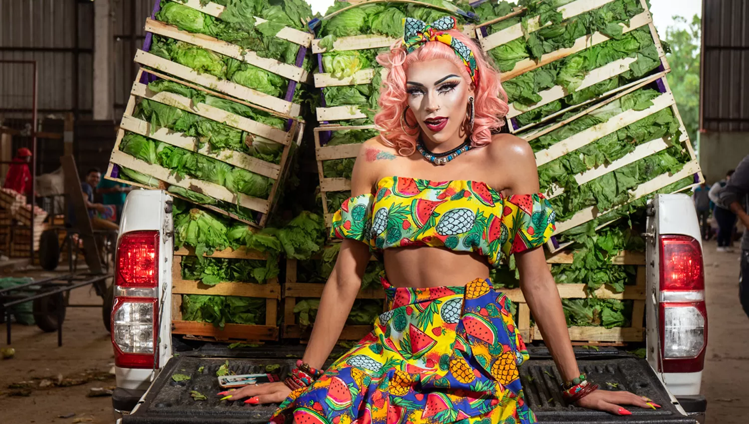 La artista drag queen Molotok posó delante de cajones de lechugas en una sesión de fotos colorida en el Mercofrut. 
