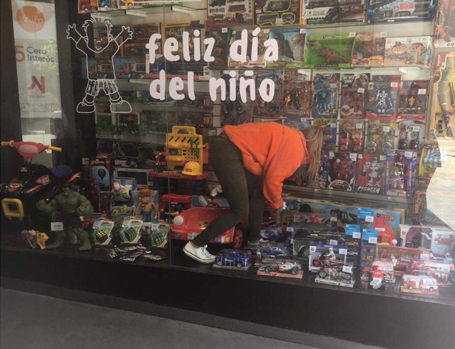 Empleada de una juguetería en peatonal Muñecas sacando los precios de la vidriera.