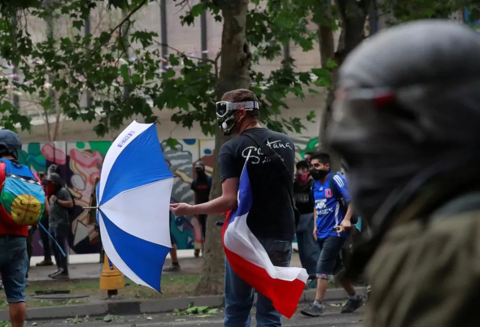 CUBIERTO. Un manifestante enmascarado abre un paraguas durante una protesta en Santiago de Chile. Reuters