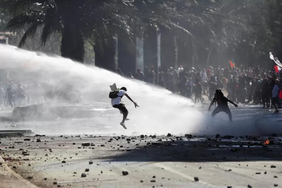 ENTRE CHORROS Y PEDRADAS. Manifestantes intentan esquivar el agua de un camión hidrante durante las violentas protestas de ayer en la capital. 