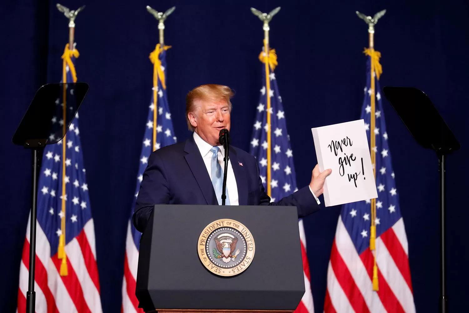 JÁMAS DARSE POR VENCIDO. Eso es lo que dice el cartel que tiene Trump en la mano. REUTERS