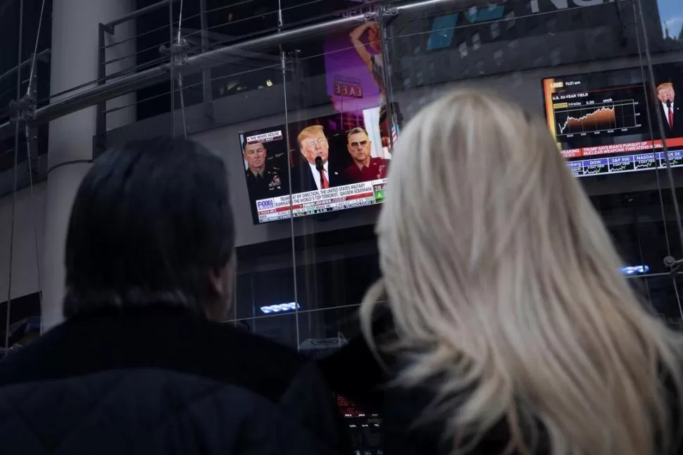 NUEVA YORK. Peatones escuchan al presidente Donald Trump que habla desde la Casa Blanca; su imagen aparece en las pantallas de Times Square. reuters