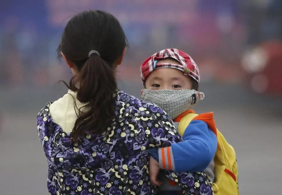 CUIDADOS. Un niño chino con barbijo en brazos de su madre. 