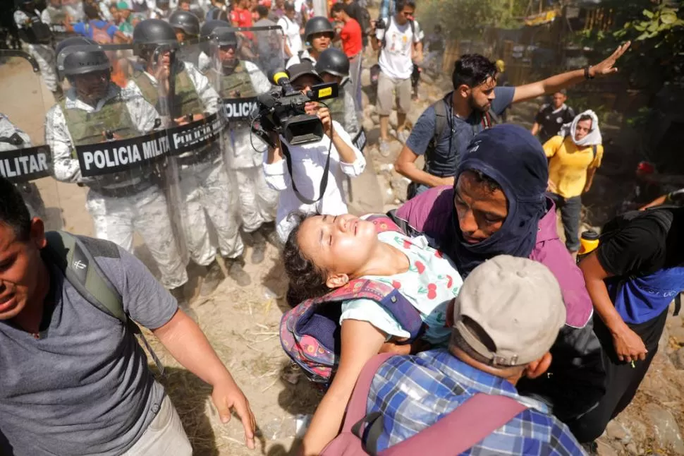 REPRESIÓN. Un grupo de migrantes carga a una niña que se ha desmayado y que no ha logrado traspasar el bloqueo de la Guardia Nacional.   reuters