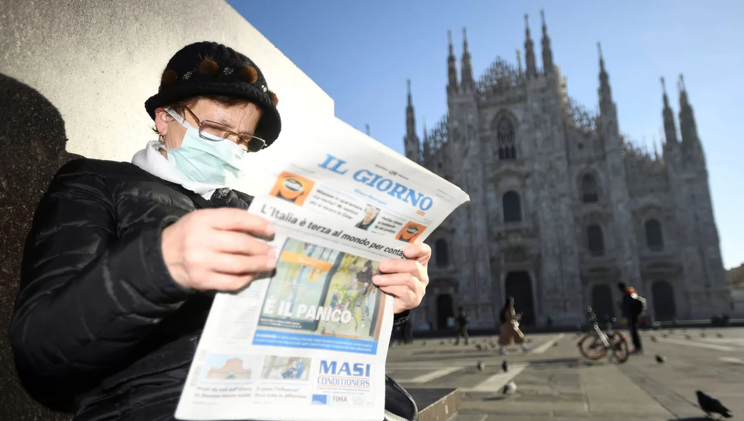 CALLES VACÍAS. Una mujer, con barbijo, lee noticias en las afueras del duomo de Milán, que está desierto.