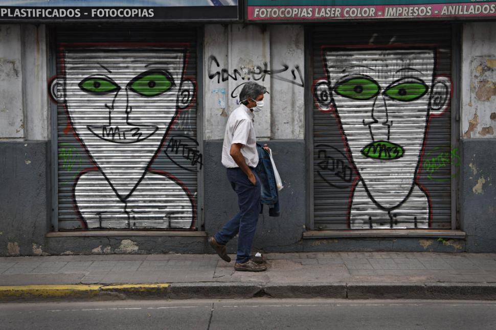 LA CIUDAD QUE  NOS MIRA. Un hombre camina por Crisóstomo al 700; de fondo aparecen los inquietantes grafitis de un negocio cerrado. 