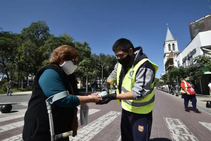 ALCOHOL EN GEL. Un agente ayuda a una mujer con muletas a higienizar sus manos en la plaza principal.