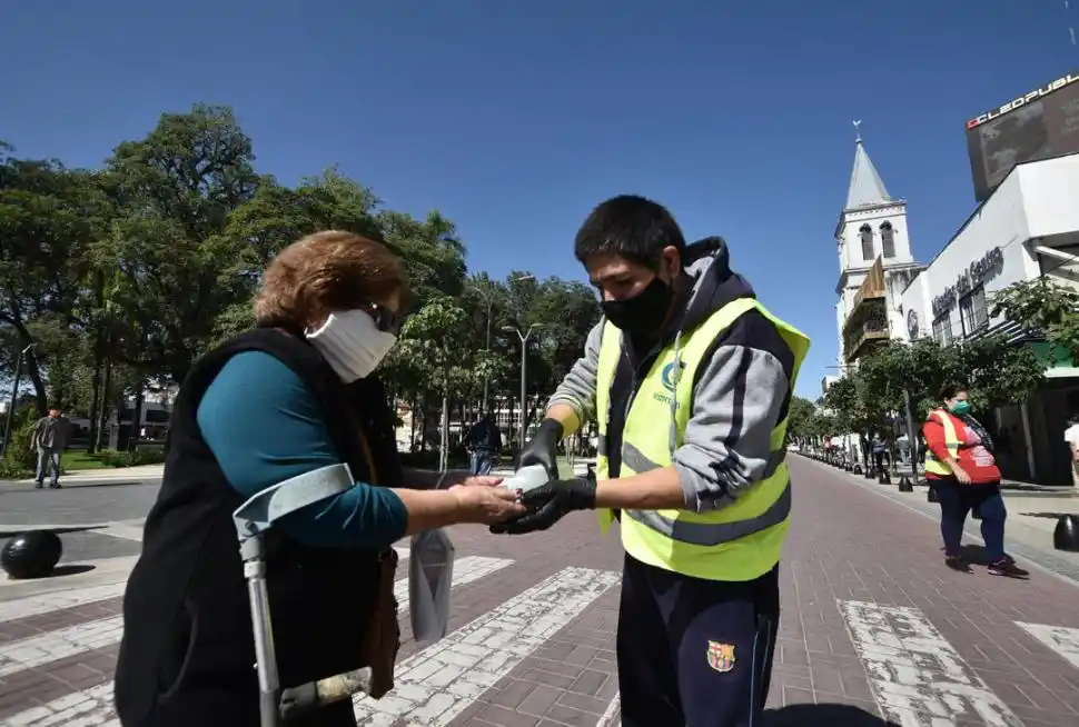 ALCOHOL EN GEL. Un agente ayuda a una mujer con muletas a higienizar sus manos en la plaza principal.