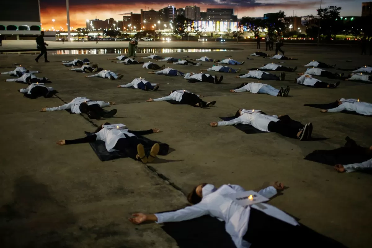 Las enfermeras con mascarillas protectoras yacen en el suelo con carteles con los nombres de los profesionales de la salud que murieron a causa de la enfermedad por coronavirus en Brasil. REUTERS