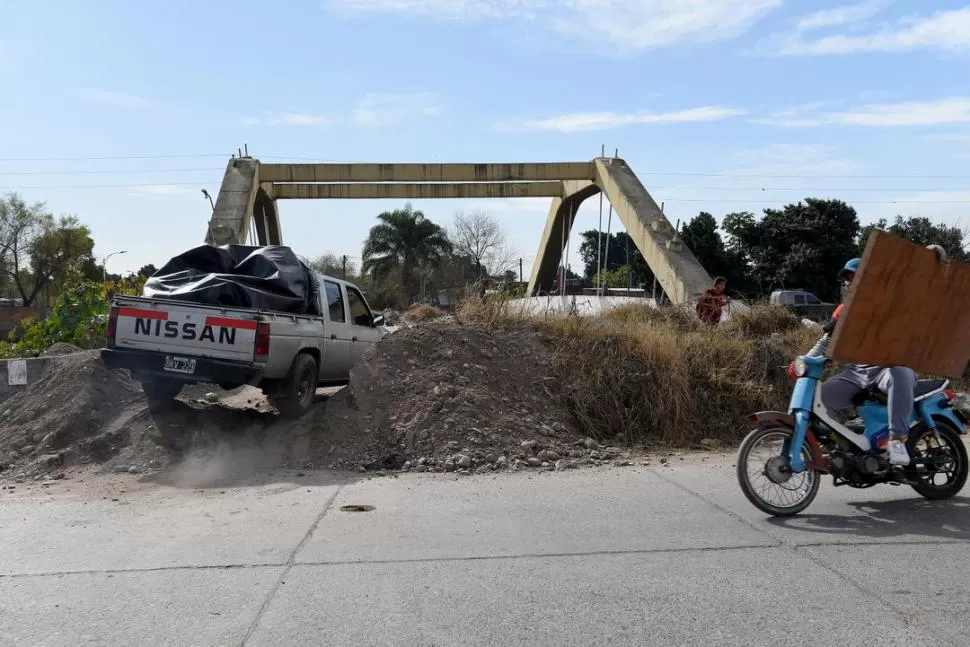 “TUCULANDIA”. Una camioneta pasa por encima del terraplén que se colocó para evitar que los vehículos crucen por el puente, ya que su gemelo se derrumbó en 2018. Mientras, un hombre carga una madera sobre una moto. la gaceta / Fotos de José Nuno