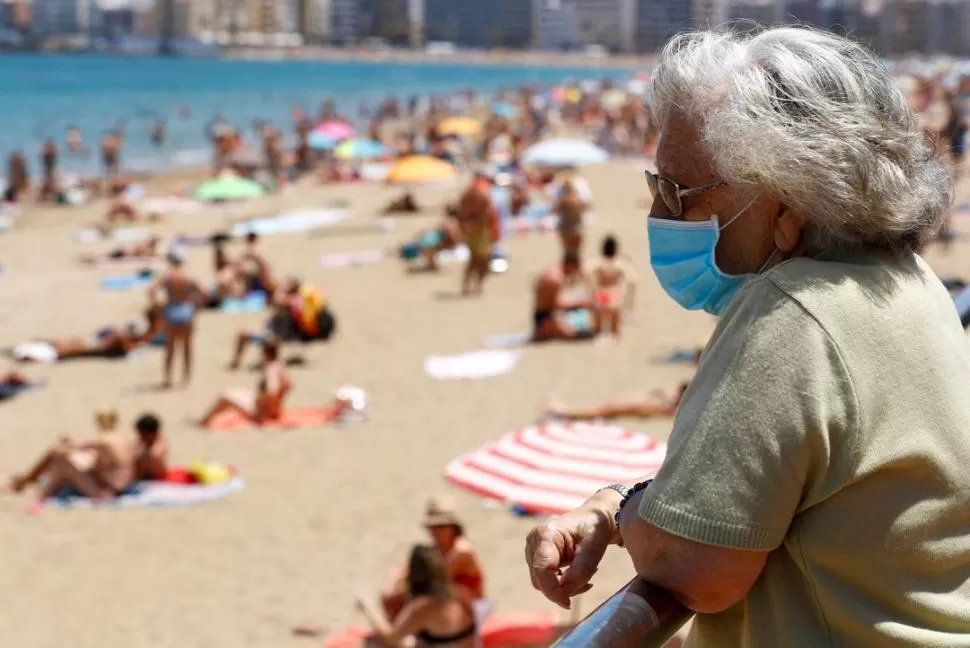 LAS PALMAS. Una mujer, con barbijo, observa a quienes descansan en la playa. En España el temor no decrece. 