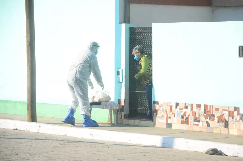 CUBIERTO. Un agente municipal deja las provisiones a una vecina en la zona aislada de Lastenia. Foto: Prensa BRS