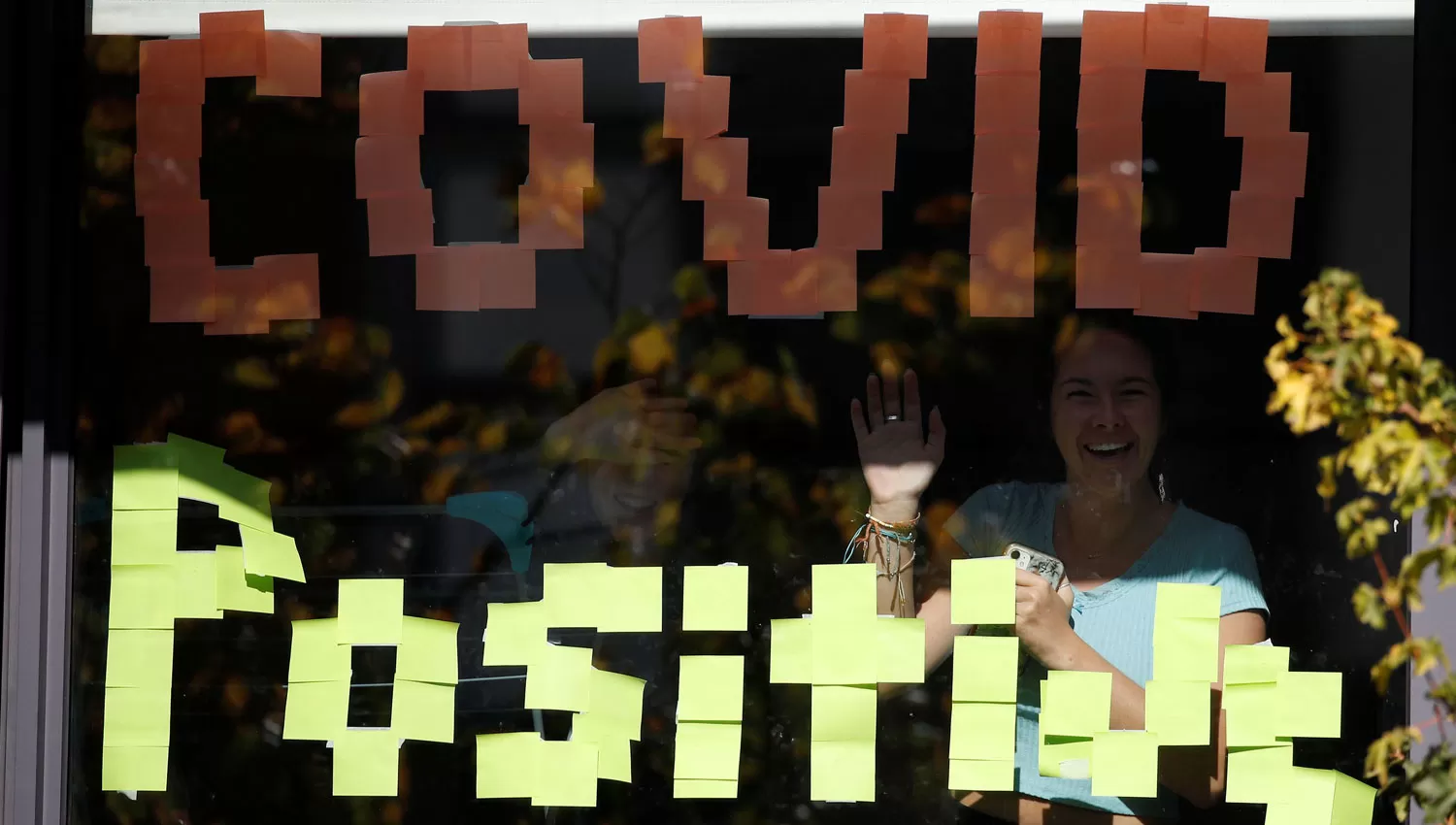 EN MANCHESTER. Una mujer saluda detrás de un cartel de covid positivo instalado en las ventanas de una residencia para estudiantes.