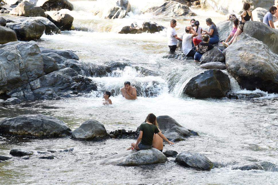 AMIGOS. Detrás, un grupo de tucumanos disfruta la tarde, charla y solo se moja un poco en el río. Al centro, un niño y un adulto juegan sumergidos hasta el pecho y la cintura. Más cerca, una pareja en una piedra. 