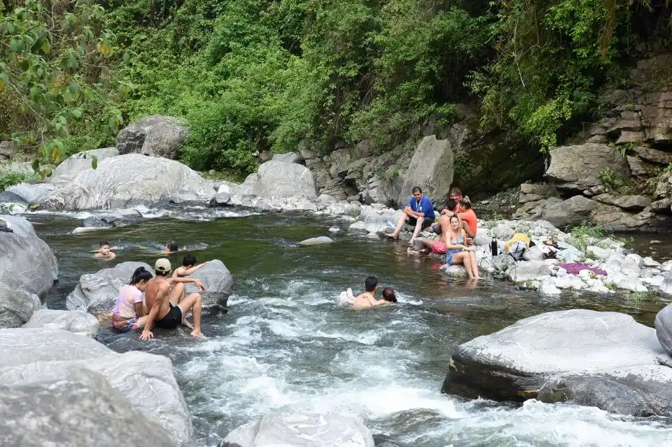 DISTANCIA Varias personas agrupadas de a dos o tres en una parte del río. Las grandes piedras hacen de mesas lejos de la ciudad.