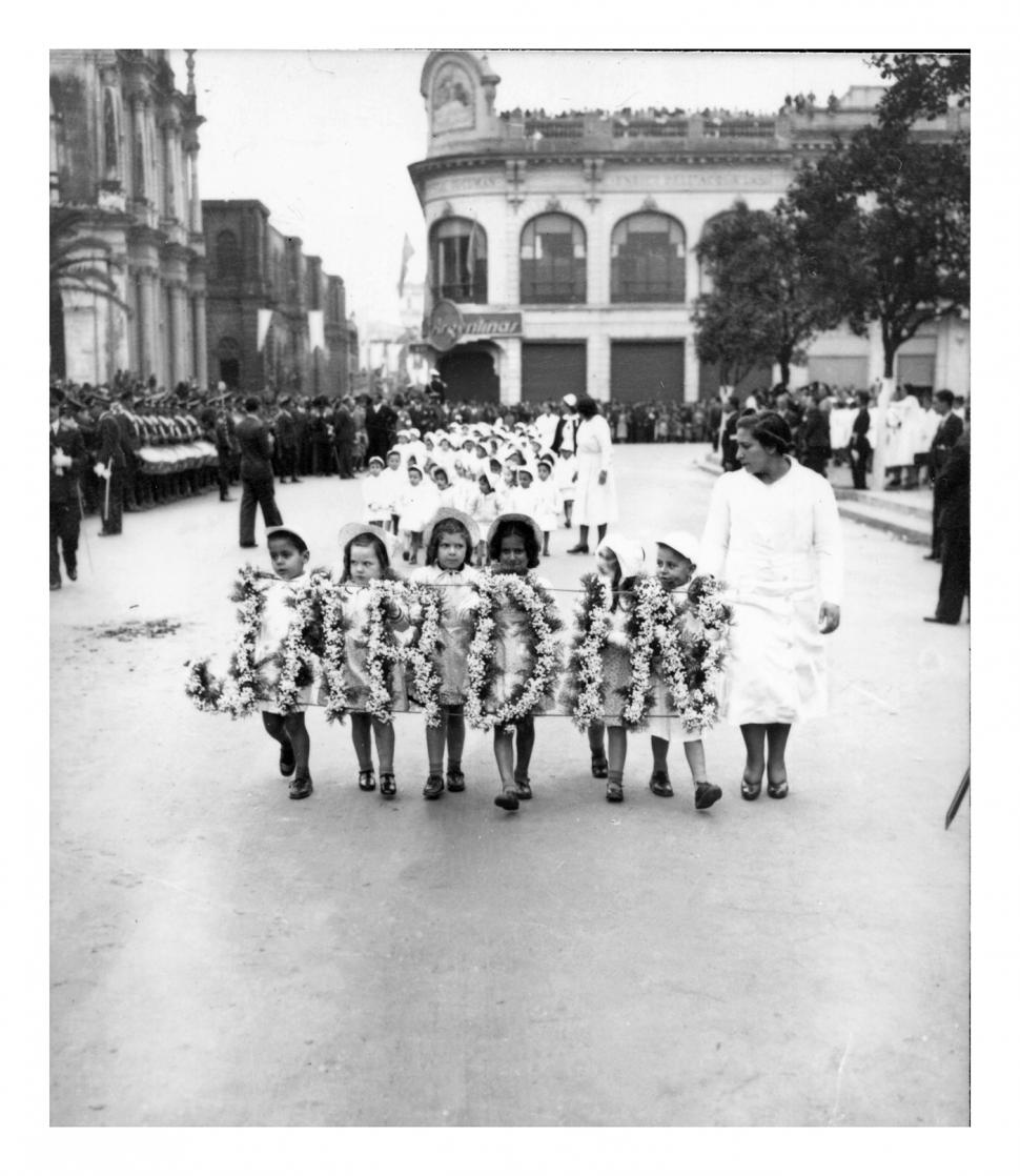  En los años treinta, los días de fiesta se realizaban desfiles alrededor de la plaza principal. Estos incluían dotaciones escolares y jardines de infantes, como la que vemos aquí, en calle 25 de Mayo, frente a casa de Gobierno. Detrás se distinguen los edificios de la iglesia San Francisco y Tiendas Argentinas.