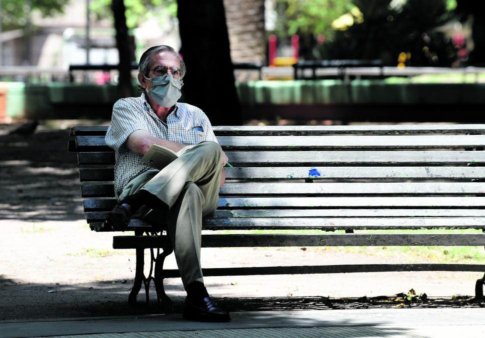 LEYENDO EN LA PLAZA ALBERDI. De riguroso barbijo, solo, sentado en la punta del banco que le escapaba al sol, este hombre usa su tiempo libre para disfrutar de la lectura de un libro.
