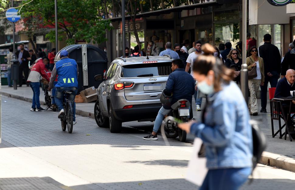 UN POCO DE TODO. La transeúnte cruza distraída mirando su celular;  el motociclista está detenido con el casco en el codo (¿se lo pondrá al circular?) y el auto está detenido en una zona restringida. 