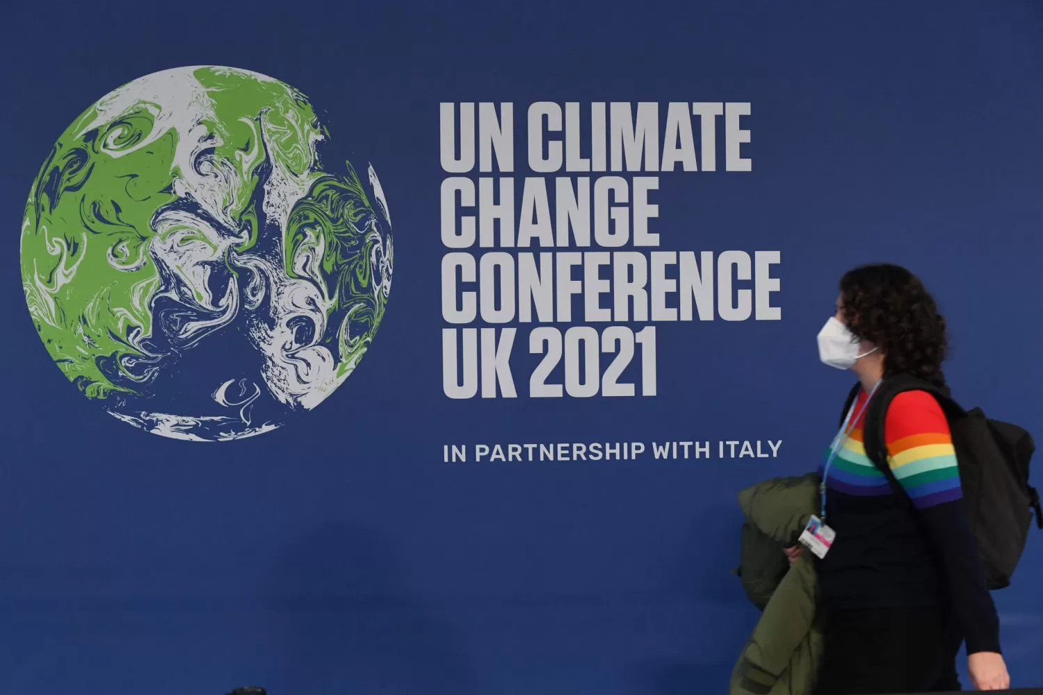 EL CAMBIO DEBE EMPEZAR. Una ciudadana camina frente a un cartel que anuncia la cumbre del clima que se celebra en Glasgow. AFP