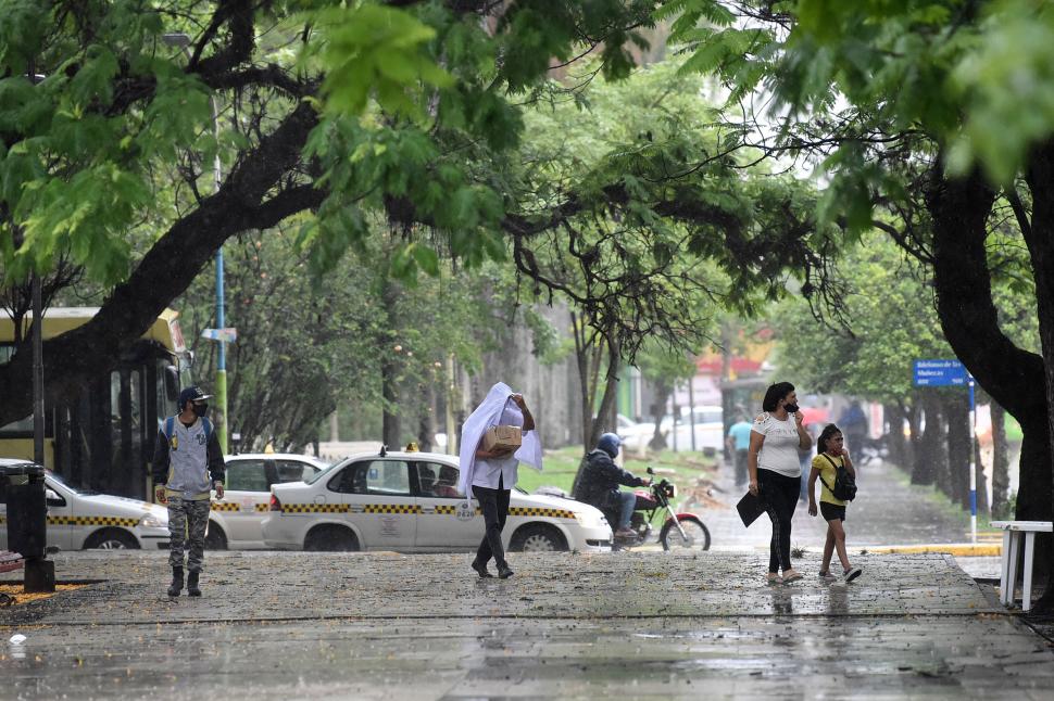 CHAPOTEANDO SIN PROBLEMAS. Mientras una persona se cubre (al centro) una mujer y una niña y un joven (izquierda) caminan sin preocuparse.