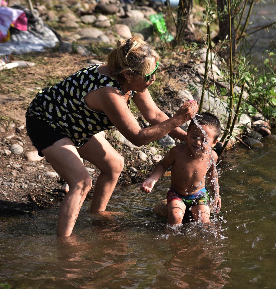 CUIDADOS. Una mujer moja a su pequeño hijo con agua del río para evitar un posible golpe de calor.