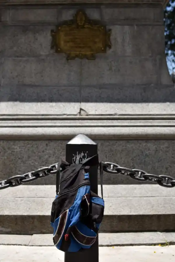 PERCHERO. En un poste del perímetro de la Estatua de la Libertad cuelgan una mochila y pegan calcos. 