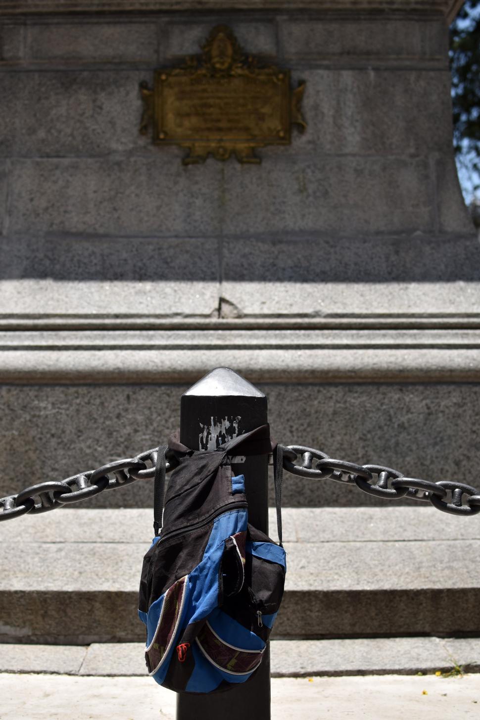 PERCHERO. En un poste del perímetro de la Estatua de la Libertad cuelgan una mochila y pegan calcos. 