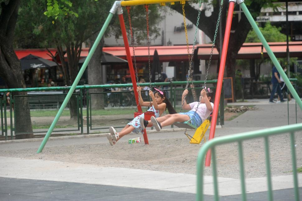 JUEGOS INFANTILES EN LA PLAZA URQUIZA. Dos niñas se hamacan en el espacio público más popular de Barrio Norte. Atrás, los bares de la Santa Fe. 