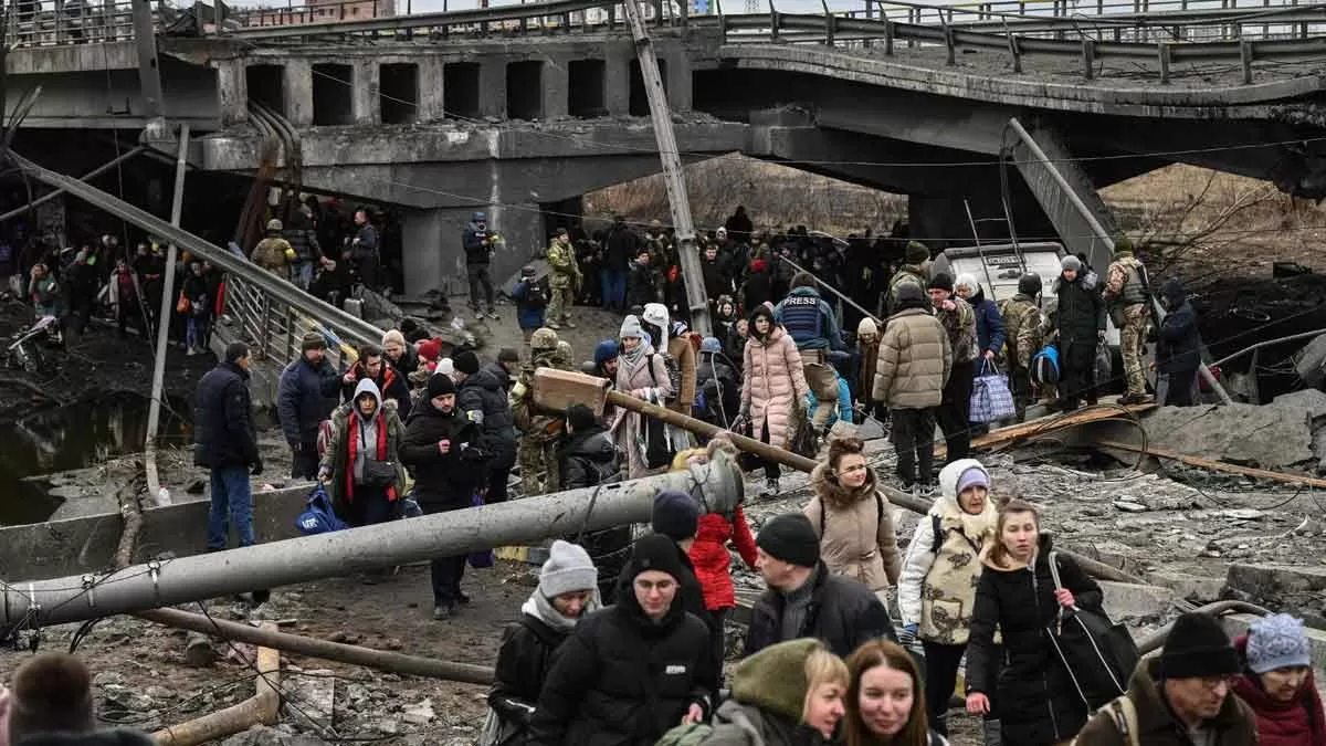 Un numeroso grupo de gente cruza un puente destruido en su camino por salir de la ciudad de Irpin, al noroeste de Kiev. / AFP