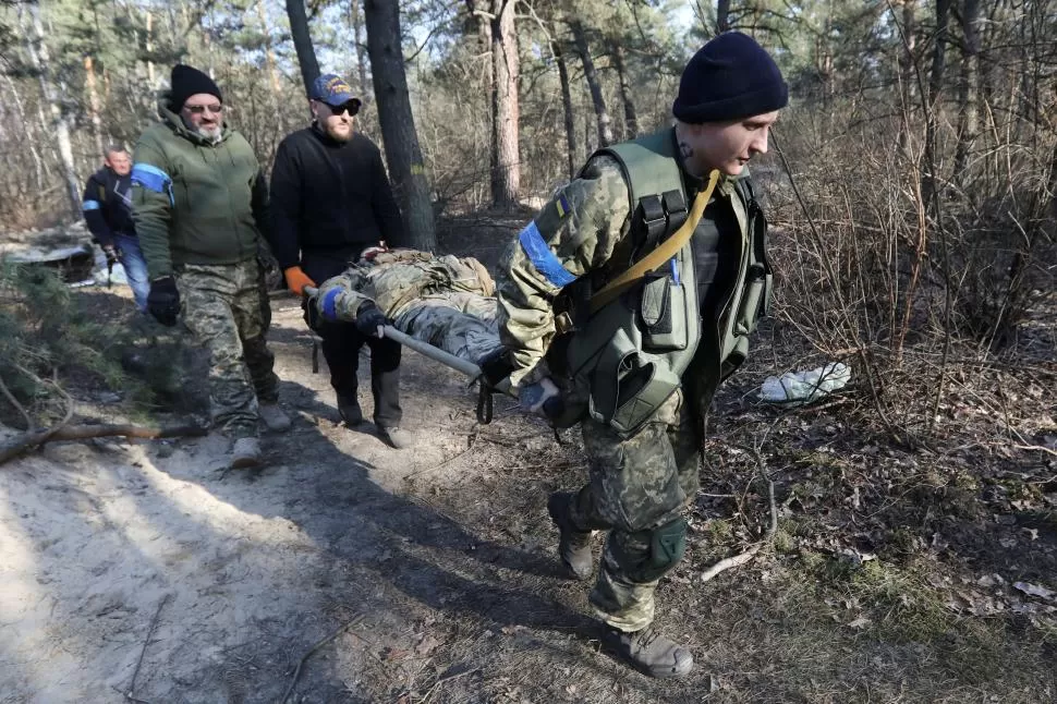 EVACUACIÓN. Miembros de las fuerzas de defensa territorial de Ucrania transportan a los heridos cerca de Kiev. 