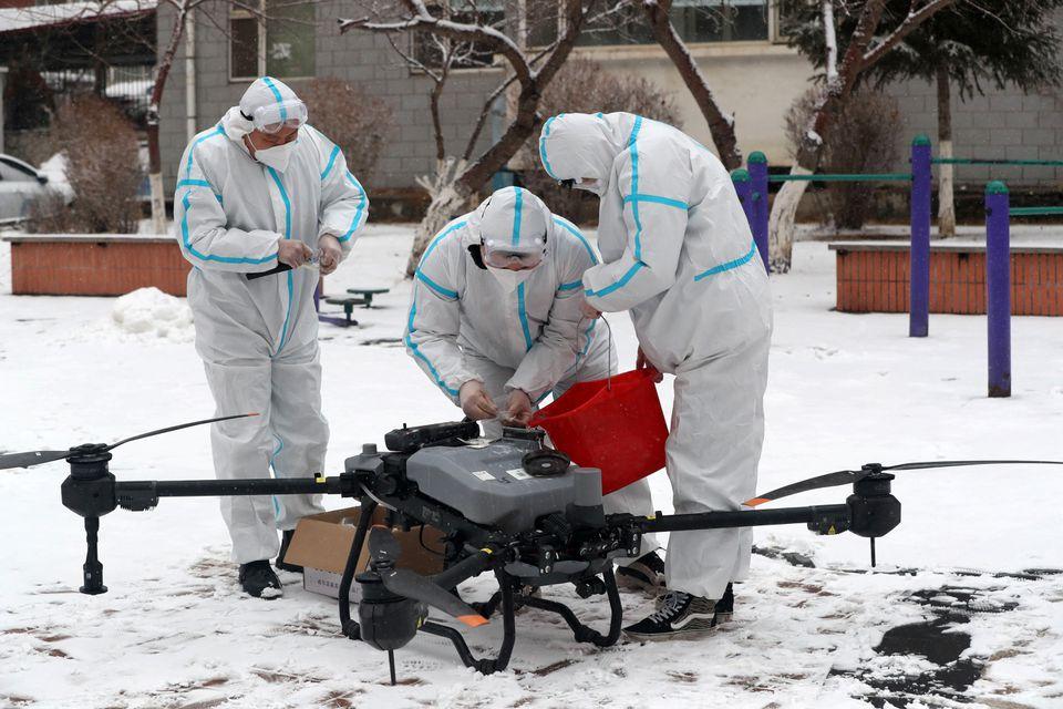 Trabajadores con trajes protectores preparan un dron en medio de la nieve para desinfectar un complejo residencial bajo encierro, luego del brote. Foto de Reuters
