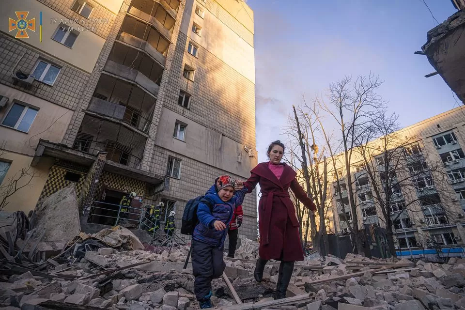 Una mujer con un niño evacua de un edificio residencial dañado por los bombardeos, mientras continúa el ataque de Rusia contra Ucrania, en Kiev. Foto de Reuters