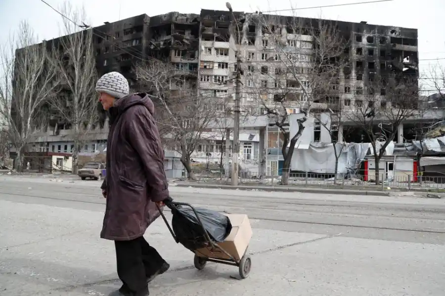 Una anciana cruza una calle cerca de un edificio dañado durante el conflicto entre Ucrania y Rusia en la ciudad portuaria sureña de Mariupol.