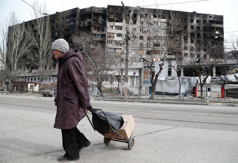 Una anciana cruza una calle cerca de un edificio dañado durante el conflicto entre Ucrania y Rusia en la ciudad portuaria sureña de Mariupol.