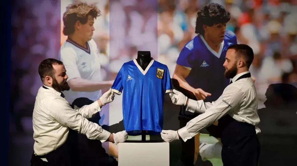GRAN MOMENTO. Dos asistentes acomodan el preciado objeto previo a la ofertas; atrás, las imágenes de los jugadores que hicieron el intercambio en 1986. 