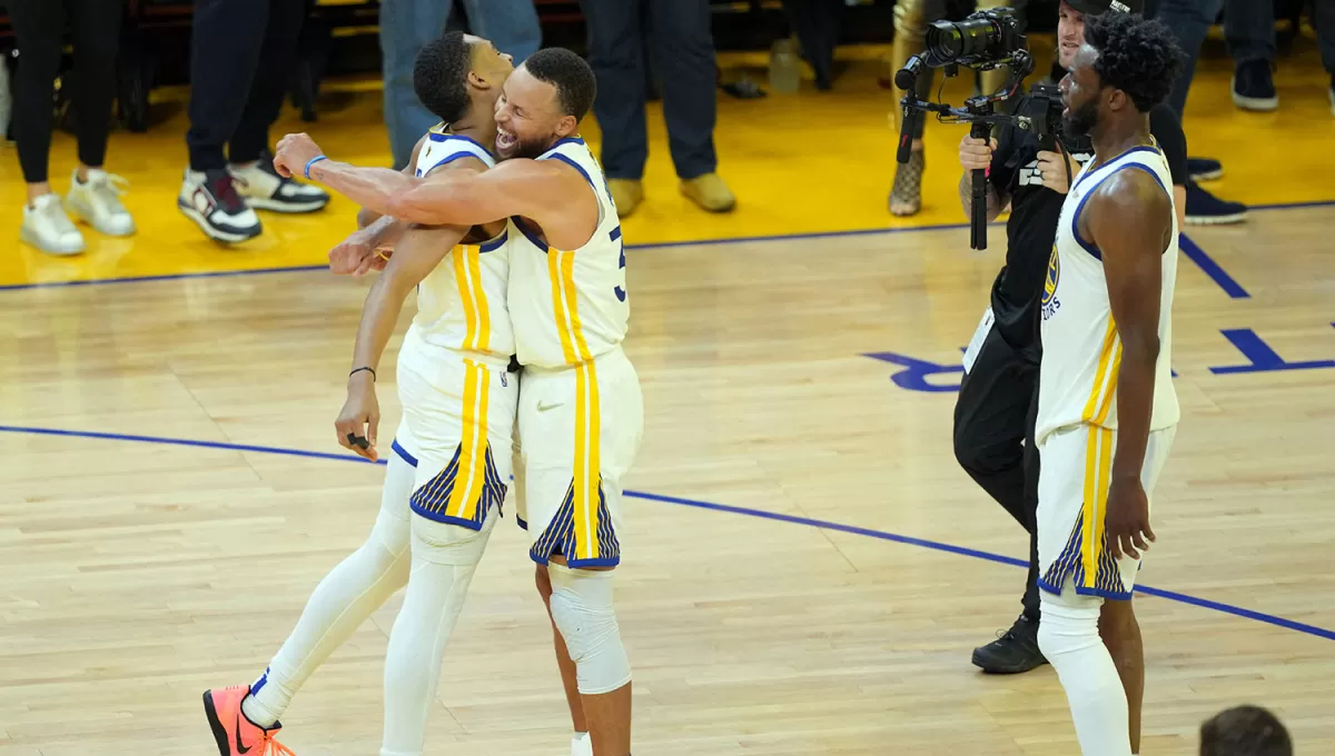 CELEBRACIÓN. Poole y Curry se abrazan mientras Wiggins sigue la escena en el Chase Center de San Francisco.
