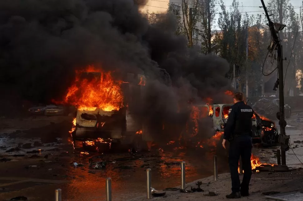 EN LLAMAS. Un policía observa cómo se incendia un vehículo tras el bombardeo ruso con misiles en la capital ucraniana. 