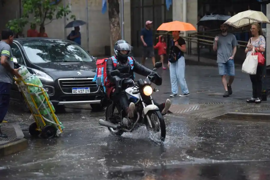 DE VEREDA A VEREDA. Un repartidor de comida intenta no mojarse más de lo inevitable en su recorrido.